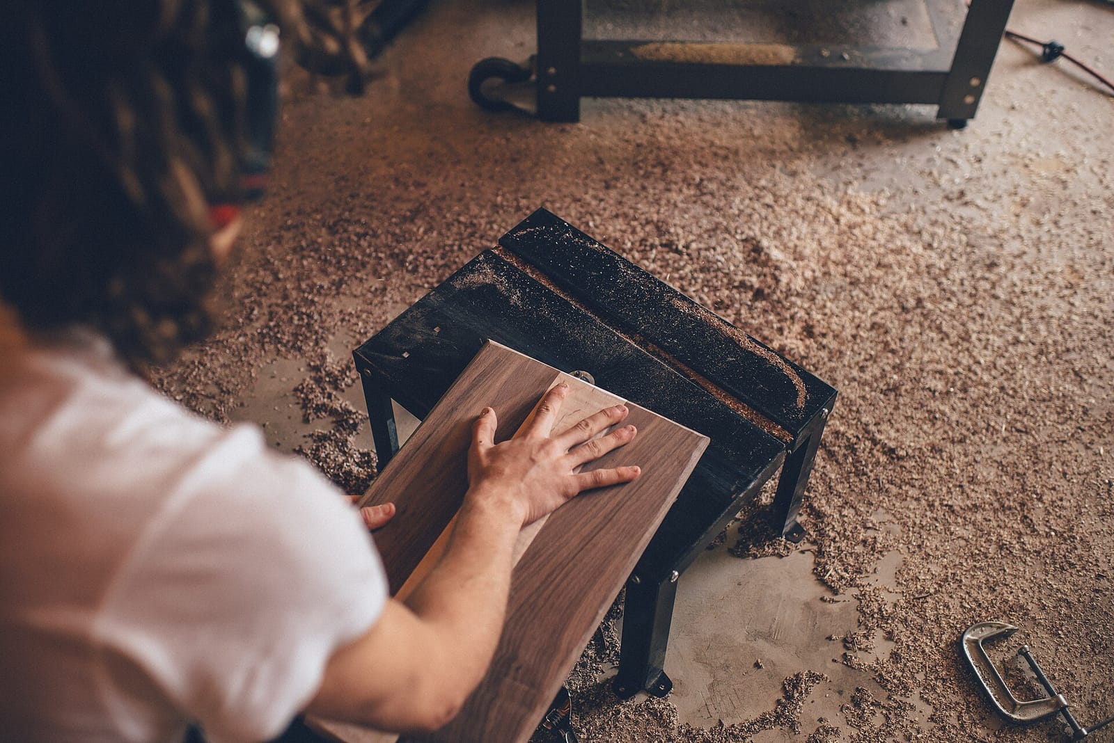 A woodworker sanding a board in a workshop full of sawdust
